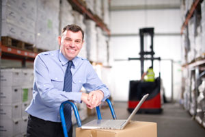 Manager with laptop on a box in a warehouse